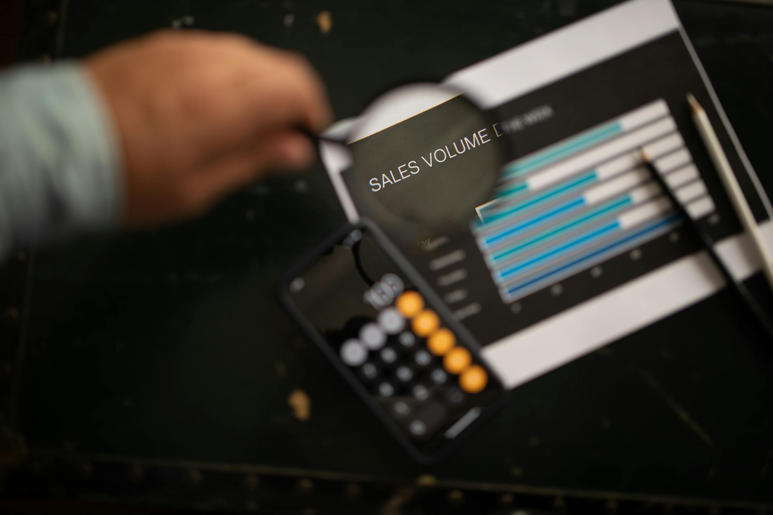 A focused examination of sales volume data using a magnifying glass and calculator.
